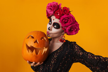 Amusing girl in halloween makeup taking selfie while posing with pumpkin
