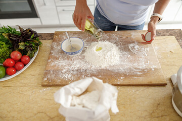 Beautiful smily handsome woman is preparing tasty fresh italian pizzawith vegetables at her kitchen at home