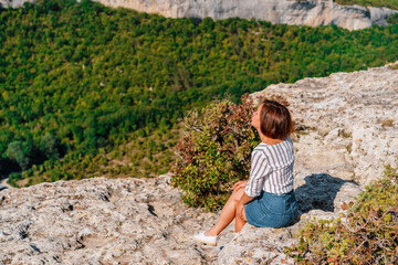 Naklejka premium A beautiful woman stands on a high cliff, enjoying the view of the mountain range and forest