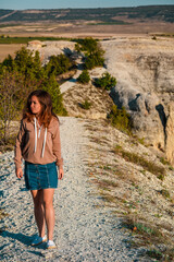 Young woman in jacket walking on narrow path on mountain range