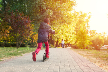 Child on kick scooter in park. A boy is riding on the kick scooter in a park.  The concept of a healthy lifestyle. Kids sport