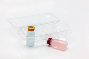 Two different colors vaccine bottle inside and one outside an opened translucent plastic box for ten vaccine bottles