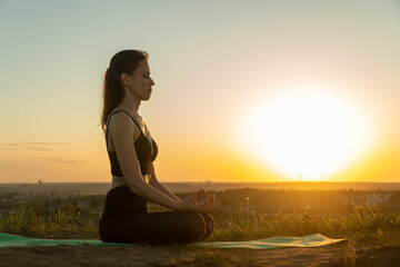 Young woman meditating in a yoga lotus pose on nature at sunset