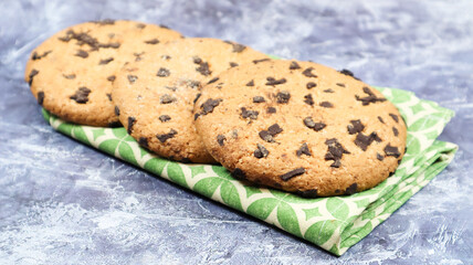 American chocolate chip cookies on a green napkin on a gray background. Traditional round crispy dough with chocolate chips. Bakery. Delicious dessert, pastries.