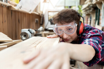 Young attractive 30-40 professional female carpenter looking grinding raw wood with sandpaper in carpentry diy workshop. Feminine women equality concept. Adult girl with male hobby at workbench