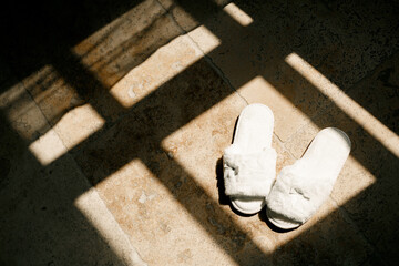 Obraz na płótnie Canvas White indoor fluffy women's slippers in the room in the sun.