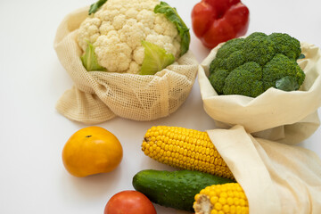 Vegetables in eco bag on white surface. Pepper, tomato, corn, cucumber, broccoli, cauliflower in reusable shopping eco friendly cotton fabric bags. Zero waste and plastic free concept. Sustainable.