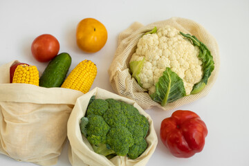 Vegetables in eco bag on white surface. Pepper, tomato, corn, cucumber, broccoli, cauliflower in reusable shopping eco friendly cotton fabric bags. Zero waste and plastic free concept. Sustainable.