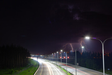 night clouds with lightning over the night track, the track is illuminated by street lights
