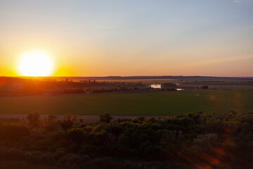 sun sets over the horizon against the backdrop of green fields and forests