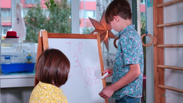 A teenager gives mathematical knowledge to a child on a flipchart. The boy writes zeros numbers. Gestures, talks about numbers. Multi-age training group.