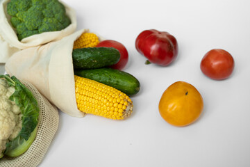 Vegetables in eco bag on white surface. Pepper, tomato, corn, cucumber, broccoli, cauliflower in reusable shopping eco friendly cotton fabric bags. Zero waste and plastic free concept. Sustainable.
