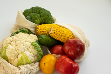 Vegetables in eco bag on white surface. Pepper, tomato, corn, cucumber, broccoli, cauliflower in reusable shopping eco friendly cotton fabric bags. Zero waste and plastic free concept. Sustainable.