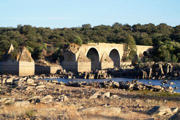 Stone river bank with a collapsed old bridge
