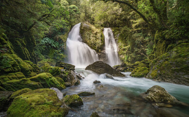 Epic waterfall in lush green mossy forest. Stewart Falls New Zealand