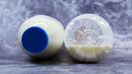 Fototapeta premium A half-empty and full plastic bottle of fresh regular milk lies on a dark gray marble or concrete backdrop. Close-up front view. World milk day concept. Nutrient fluid.