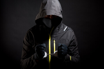 Unknown, indistinguishable thug or hucker in handcuffs and black clothes is arested. Concept: Crime because of crisis covid 19. isolated on black background