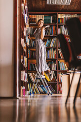 Full length of young attractive librarian standing on ladder and holding a book.