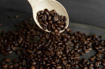 Fresh roasted arabica coffee beans falling from a oaken spoon on a wooden table.