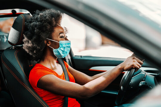 Side View Of Attractive African Woman With Short Curly Hair With Face Mask On Sitting And Driving Car. Prevention From Spreading Corona Virus / Covid 19 Concept.