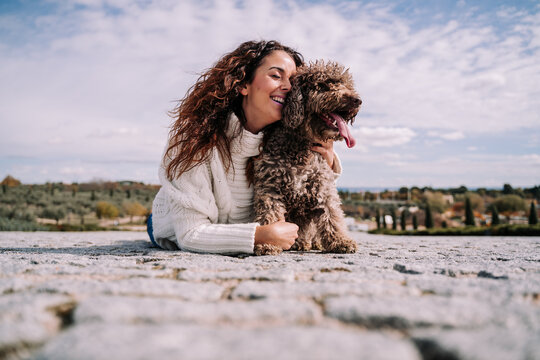 A beautiful woman lying down with her Spanish water dog in the park of Madrid. She is hugging her pet. Family dog outdoor lifestyle