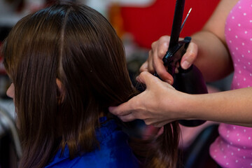 Professional female hairdresser cutting girl's brown hair in salon, closeup
