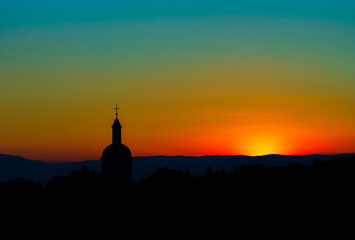 The stunning beauty and colors of the sunset overlooking the silhouettes of the Alps and the silhouette of a beautiful church