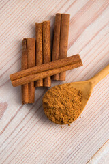 Cinnamon, whole sticks behind wooden spoon with a heap of powder