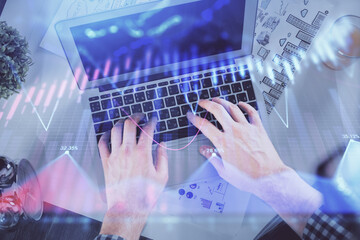 Double exposure of man's hands typing over laptop keyboard and forex chart hologram drawing. Top view. Financial markets concept.