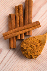 Cinnamon, whole sticks behind wooden spoon with a heap of powder