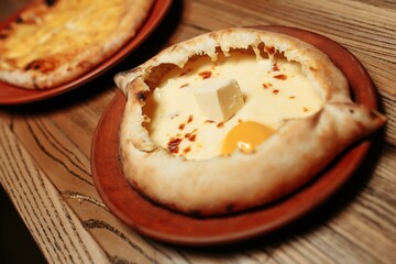Top view on traditional Adjarian Khachapuri - open baked pie with melted salt cheese suluguni and egg yolk on wooden tray. Traditional georgian food