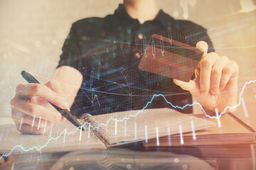Double exposure of man hands holding a credit card and Forex graph drawing. Stock trading and digital fintech in Internet E-commerce concept.