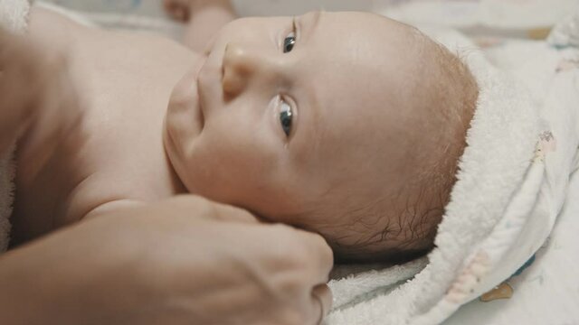 A little baby lying in bed and his mother cleaning his ears with q-tips