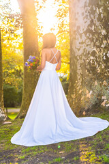 Caucasian brunette in wedding dress at sunset wedding celebration next to a tree in the park