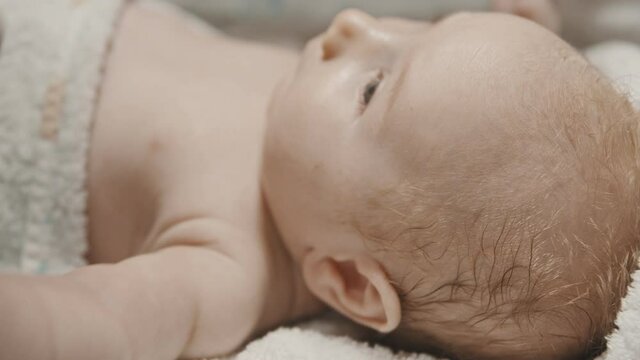 A little baby lying in bed and his parent cleaning his ears with q-tips