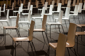 Group of empty white chairs arranged for social distance  during indoor business event. COVID-19 health and safety measures during pandemic requires spacing between people