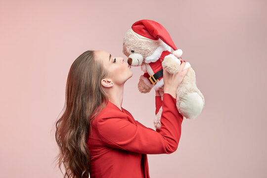 Young beautiful woman with long wavy hair kisses a toy bear in the image of Santa Claus.
