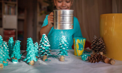 DIY craft gifts and Christmas decoration. Girl coloring cone as if it is pine tree, be green