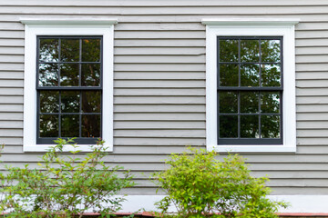 Two double hung windows with multiple panes of glass in a tan color wooden wall. The wall has...
