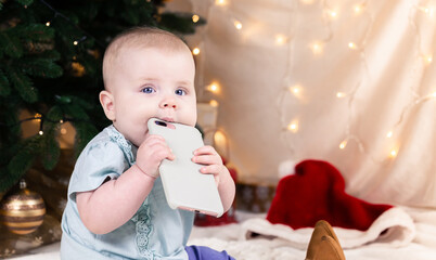 Christmas adorable small baby girl talking on the phone. Baby child portrait on the background of the Christmas tree. xmas cute toddler. Children play room.