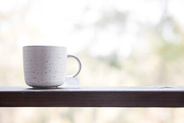 White simple ceramic herbal tea coffee mug herbal tea on a timber ledge outdoors against the blurred forest and trees natural background