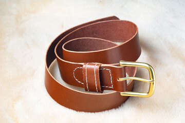 Men's brown leather belt with gold buckle on a soft surface