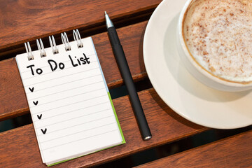 Notepad with inscription to do list sheet and coffee on wooden background.