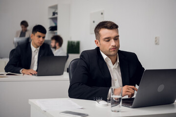 Two managers of a carsharing company are engaged in routine business in the office in a laptop. They are distracted from their work.