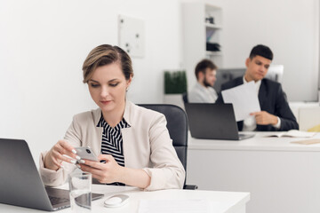 A young beautiful girl in an open space office receives a message on a social network from a colleague on her smartphone and reads it.