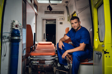 Paramedic in a blue medical uniform sitting in an ambulance car.