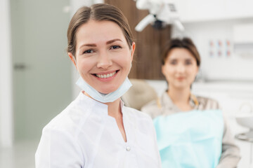 Fototapeta premium A portrait of a beautiful young doctor with her patient in the back of the picture.