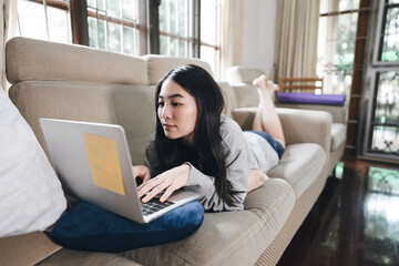 oung adult asian woman laying on sofa with laptop computer for work and online media at home