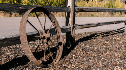 Fototapeta na wymiar Broken wagon wheel in a field laying by an old wooden fence background. Farming equipment and spoked chariot wheel rustic vintage garden decorations