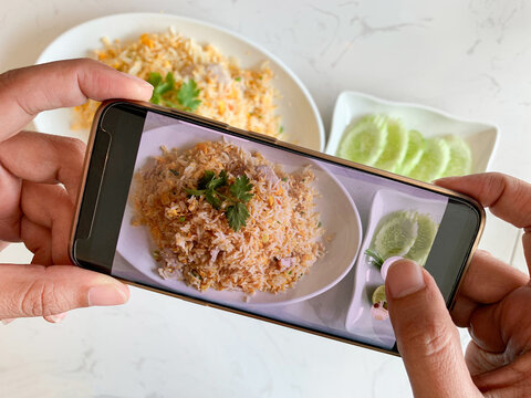 Women use smartphones to record images of food  that are placed on the table in the kitchen.